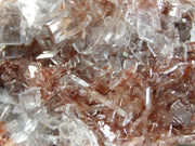 A striking mineral specimen featuring transparent, tabular celestine crystals jutting out from a rusty-red hematite-stained matrix. The crystals are glassy and well-formed, arranged in a bristling formation across the specimen's surface. The dramatic contrast between the clear, prismatic crystals and the deep red-brown matrix creates a natural sculptural effect.